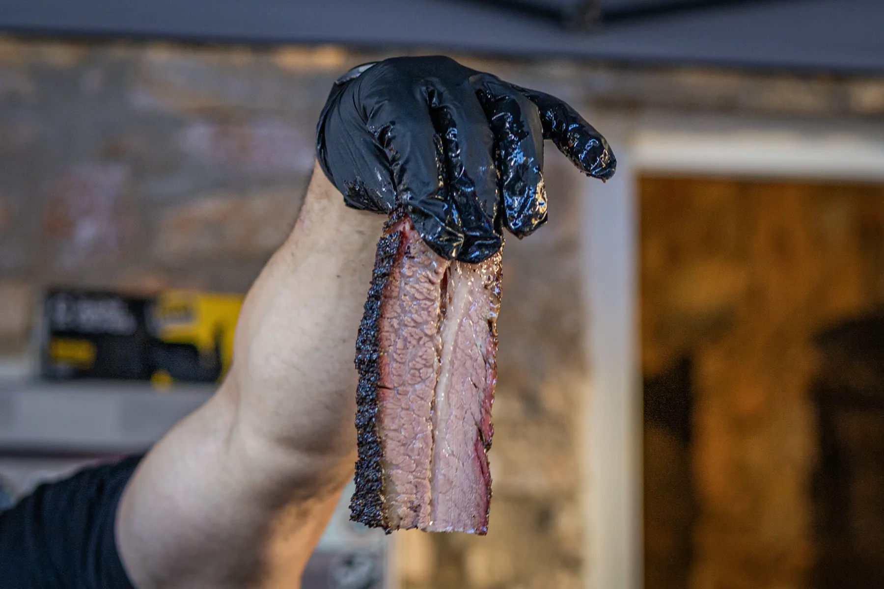 Φέτα brisket σηκωμένη με γάντι πάνω από το smoker.